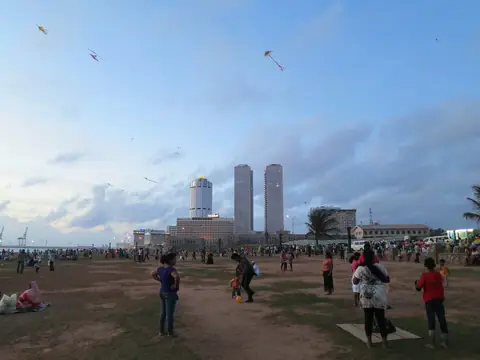 Families flying kites on Galle Face Green on a Sunday, with the city's towers behind