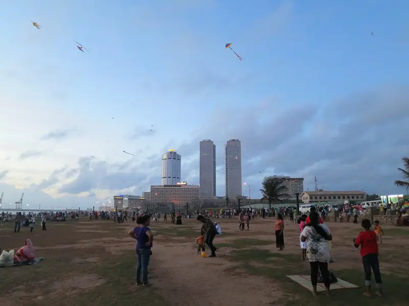 Families flying kites on Galle Face Green on a Sunday, with the city's towers behind