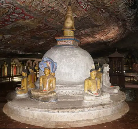 A painted stupa ringed by seated Buddhas inside a Dambulla cave