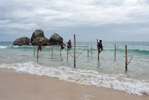 Stilt fishermen on their poles in the surf at Koggala